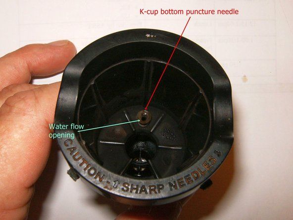 Kカップインサートの底には、Kカップの底に穴を開ける先細の針があります。その側面には小さな穴があります。ペーパークリップ（または同様のもの）を使用してそこに挿入し、スケールやコーヒーかすなどを取り除きます。' alt=