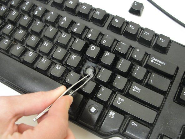 अपने कीबोर्ड पर अब खुले छेद से नीचे दबाए जाने से कुंजी को रोकने वाले किसी भी दूषित पदार्थों को हटाने के लिए चिमटी का उपयोग करें।' alt=