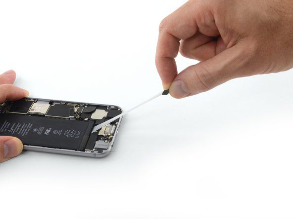 Pomalu vytáhněte lepicí poutko od baterie směrem ke spodní části iPhone.' alt=