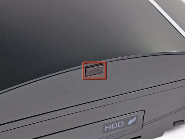 Sử dụng đầu của một spudger để tháo nắp vít cao su màu đen khỏi mặt bên của PS3.' alt=