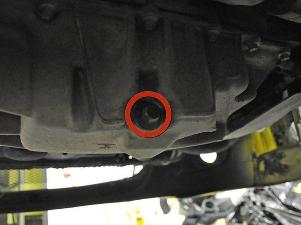 Individua il tappo di scarico della coppa dell'olio sotto l'auto. È un bullone esagonale da 13 mm rivolto verso il retro dell'auto.' alt=