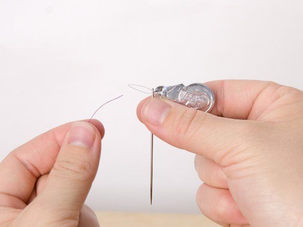 Hold både nåletråder og nål i den ene hånden mens du holder nålen på nåletråderen gjennom nåløyet.' alt=