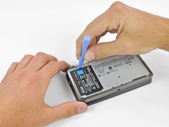 Поставете пластмасов инструмент за отваряне в прореза в долната част над батерията.' alt=