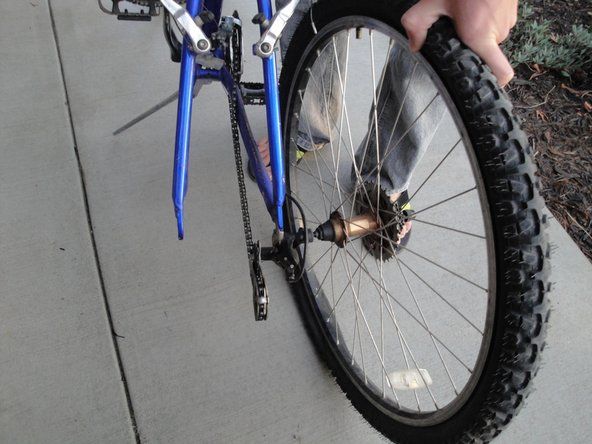 Hold hjulet i bakken, og trekk sykkelrammen opp og bort for å fjerne hjulet fra sykkelen.' alt=