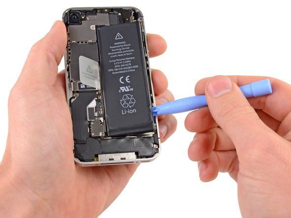 Steek de rand van een plastic openingstool tussen de batterij en de behuizing aan de onderkant van de iPhone.' alt=