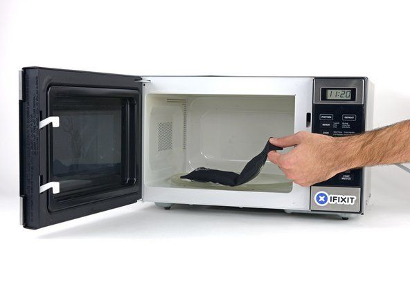 Keluarkan iOpener dari ketuhar gelombang mikro, pegang dengan salah satu daripada dua hujung rata untuk mengelakkan pusat panas.' alt=