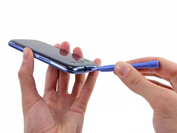 Masukkan alat pembuka plastik atau kuku ke dalam takik di celah antara casing belakang dan bagian ponsel lainnya, yang terletak di bagian atas perangkat.' alt=