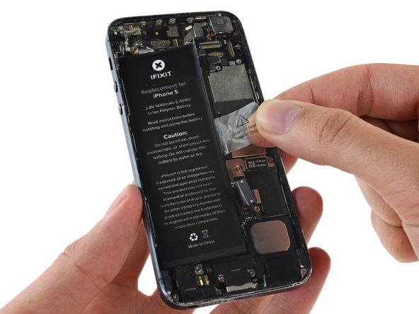 露出した透明なプラスチック製のプルタブを使用して、iPhoneに固定している接着剤からバッテリーをはがします。' alt=