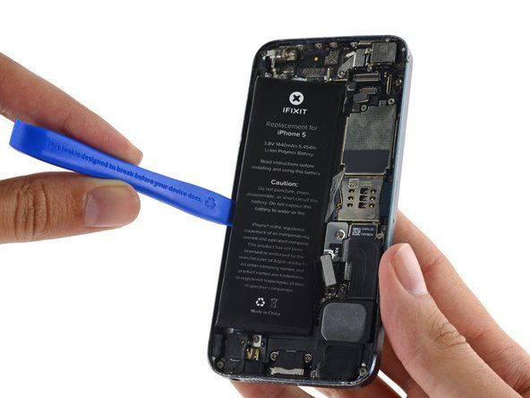 Bruk åpningsverktøyet i plast for å lirke batteriet forsiktig opp, bare ved ytterkanten av telefonen. Å nekte noe annet sted, spesielt i nærheten av logikkortet, kan føre til skade på logikkortet.' alt=