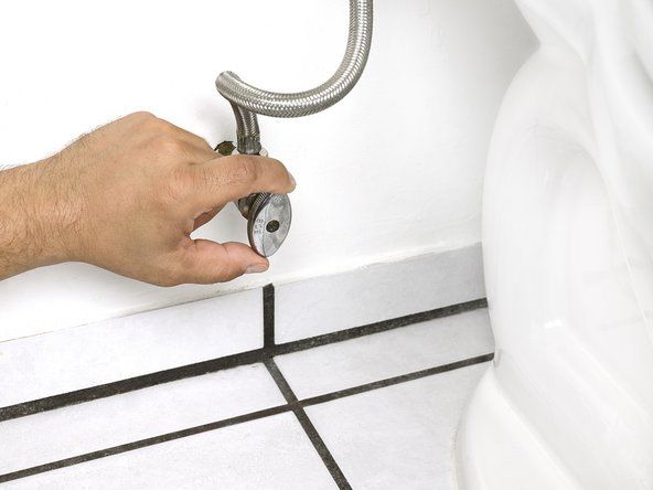 Изключете спирателния клапан под тоалетната, като го завъртите по посока на часовниковата стрелка, докато стане здраво затегнат.' alt=