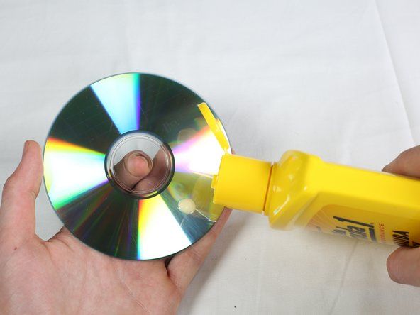 Phủ một lớp sáp xe hơi mỏng trực tiếp lên đĩa CD, sử dụng phương pháp thoa theo vòng tròn.' alt=