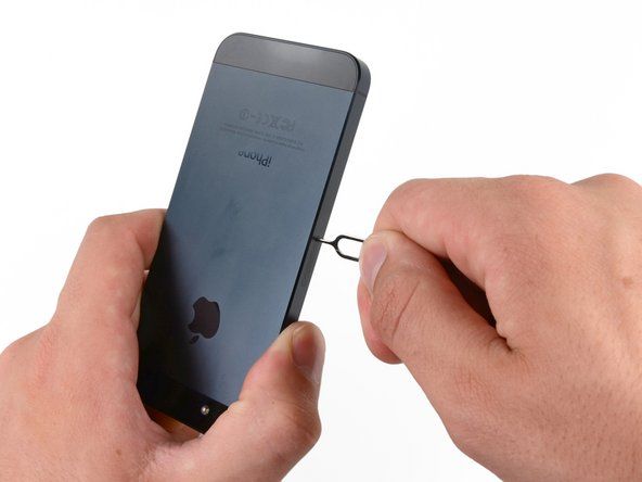 Nospiediet SIM kartes atlaišanu iPhone labajā pusē ar SIM kartes izstumšanas rīku vai saliektu saspraudes palīdzību, lai izstumtu SIM kartes paliktni.' alt=