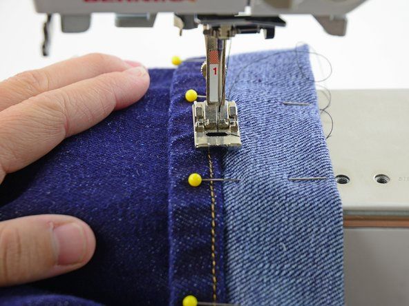 Richten Sie die Mitte des Nähfußes (und der Nadel) an der Kante des Saums der Jeans aus.' alt=