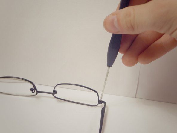 लेंस और बाहों के बीच चश्मे के कोने काज पर पेंच का पता लगाएँ और वामावर्त घूर्णन करके 1.5 मिमी पेचकश का उपयोग करके इसे हटा दें।' alt=