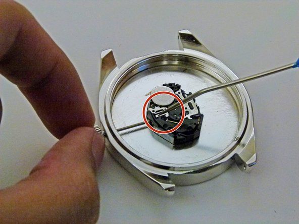 Tekan tekanan dengan instrumen ujung runcing di tempat yang dilingkari di mana batang memenuhi bahagian utama jam tangan.' alt=