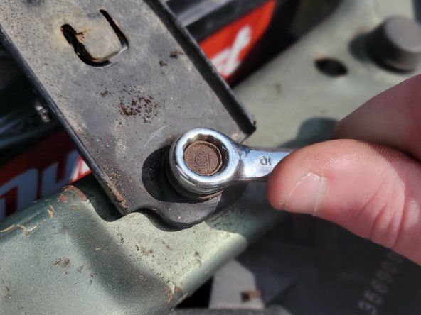 Gebruik de 10 mm moersleutel om de batterijbinder los te maken door de bout rechtsom te draaien.' alt=