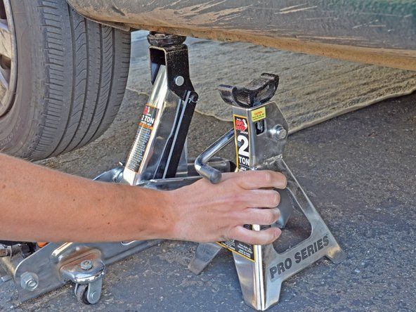 Izmantojiet domkrata statīva rokturi, lai to nolaistu un noņemiet domkrata statīvu no automašīnas apakšpuses.' alt=