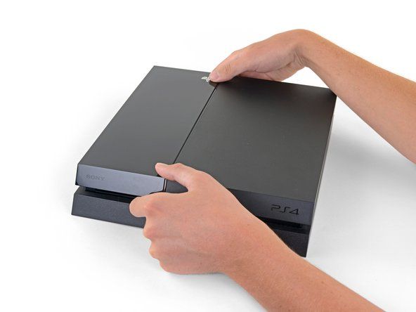 Ar abām rokām satveriet PS4 pa spraugu augšējā vāciņā.' alt=
