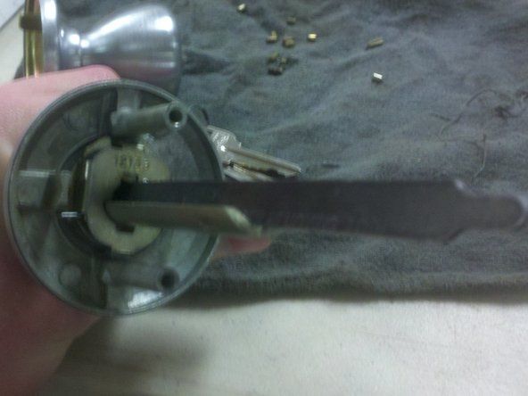Une fois la barre d'entraînement retirée, insérez l'extrémité fourchue de l'outil de retrait de cylindre à l'arrière de la serrure.' alt=