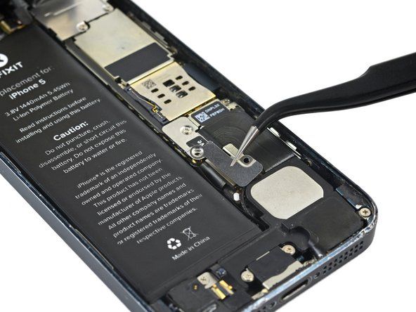 Odstranite kovinski nosilec priključka za baterijo iz iPhona.' alt=